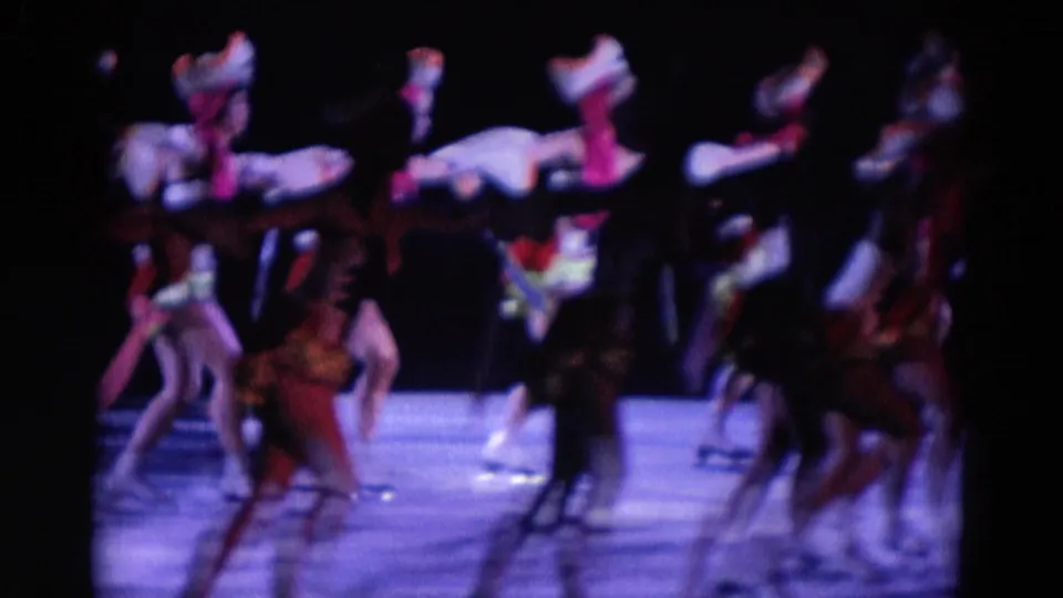 In 1969 Chicago home-movie footage, ensemble dancers appear in formation on a dark stage with saturated purple-blue light.