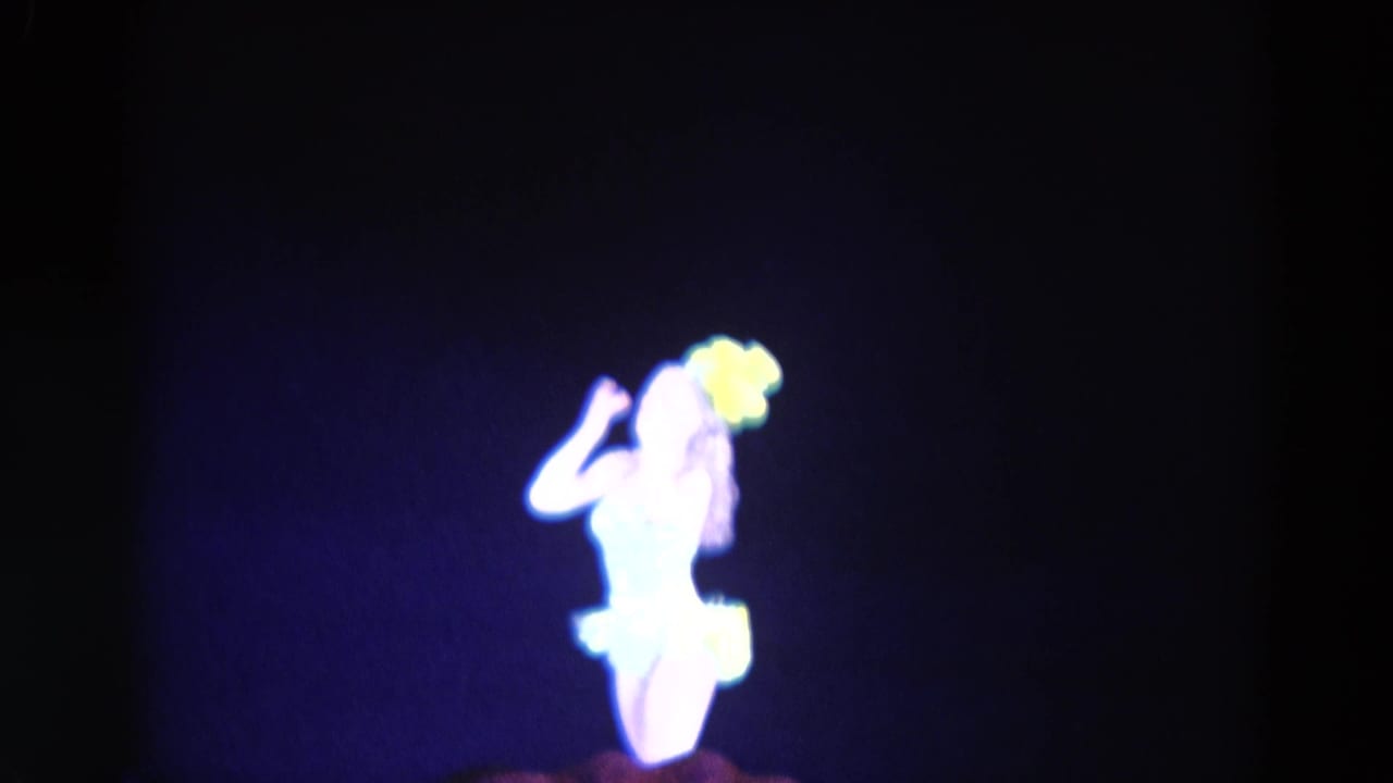 Dancer in a yellow feathered costume on a dark stage under blue light.