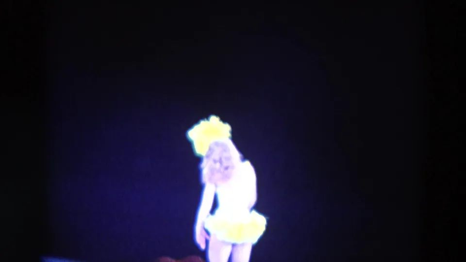 The performer dips forward in the 1969 Chicago stage scene, with yellow feathers bright against the blue-lit darkness.