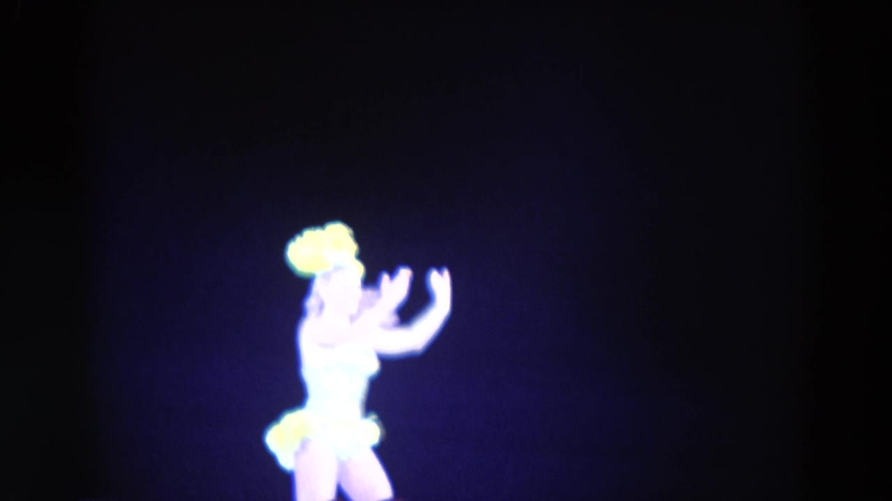 1969 Chicago 8mm frame showing a female figure skater in a bright costume with yellow accents against a dark rink background.