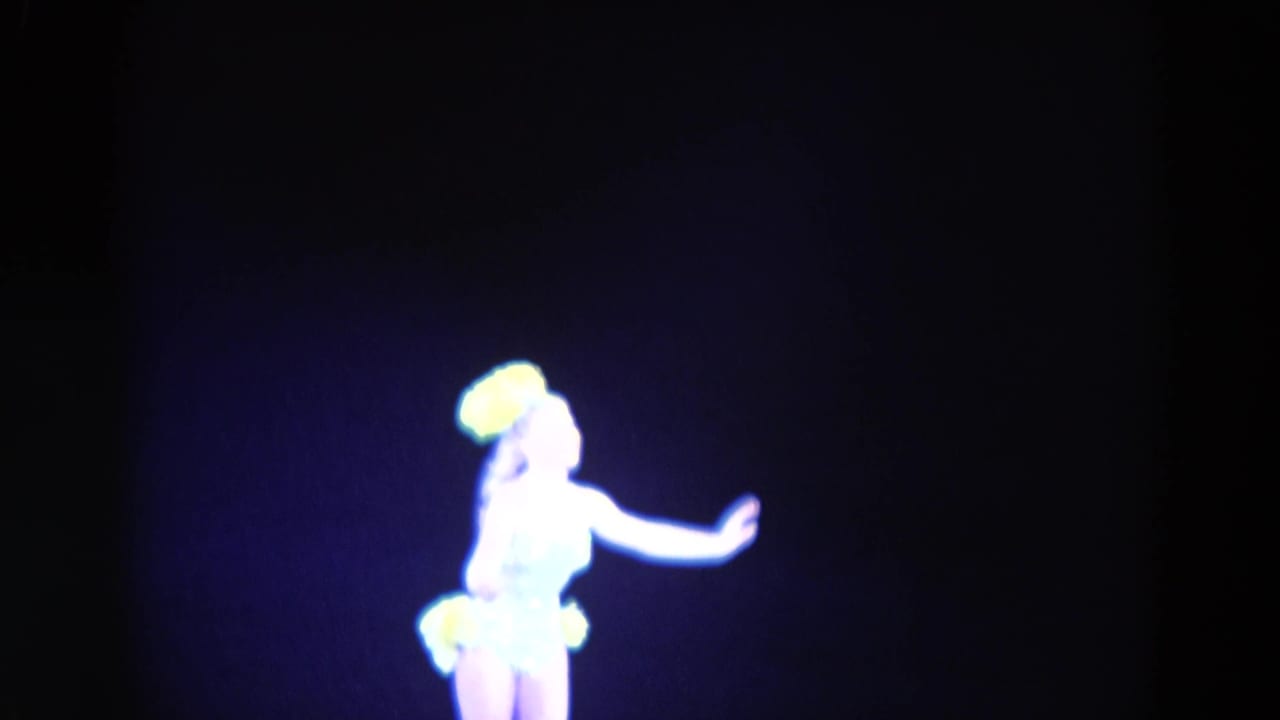 Female figure skater in a light costume and yellow headpiece appears mid-routine in the 1969 Chicago skating footage.
