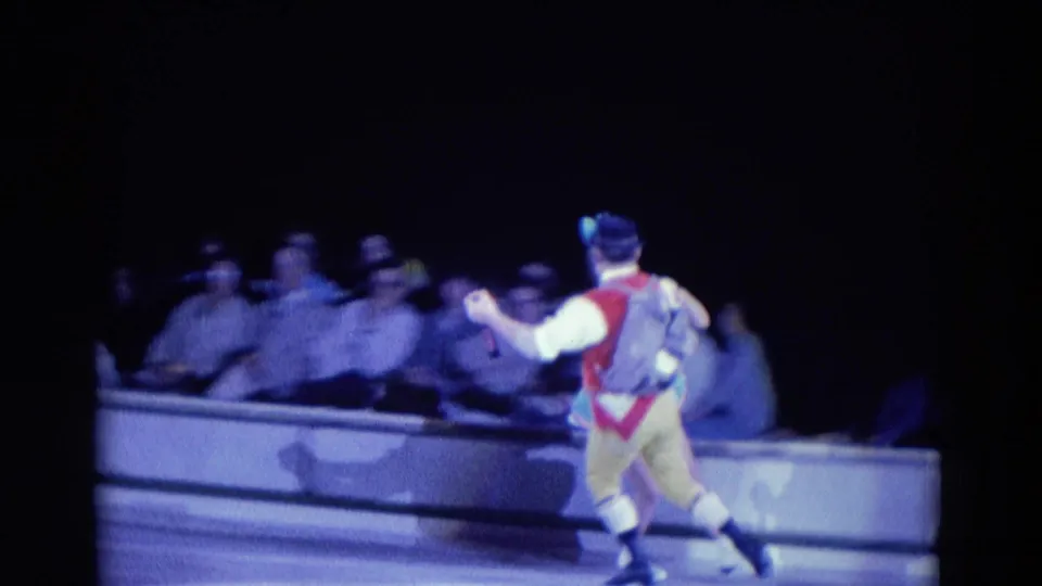 Male figure skater in colorful costume glides near seated spectators during the 1969 Chicago skating routine.