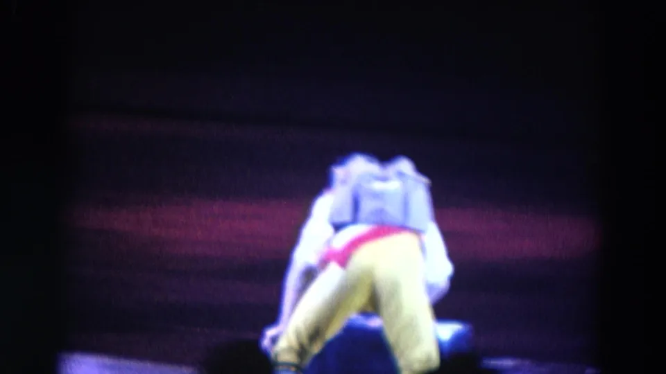 The costumed male skater bends forward with his back to the camera, lit by blue and red stage tones in Chicago footage from 1969.