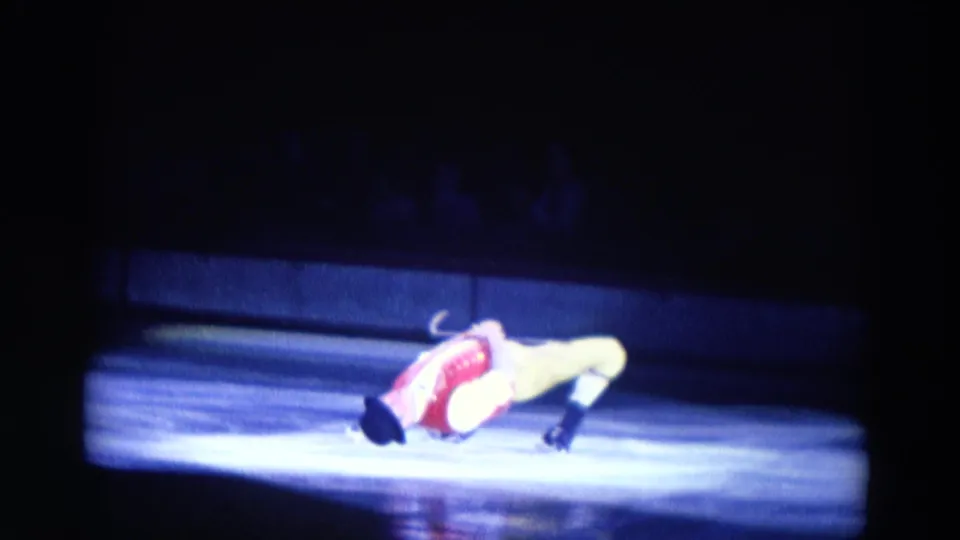 In 1969 Chicago 8mm footage, a costumed male ice performer holds a deep backbend under blue stage lighting.