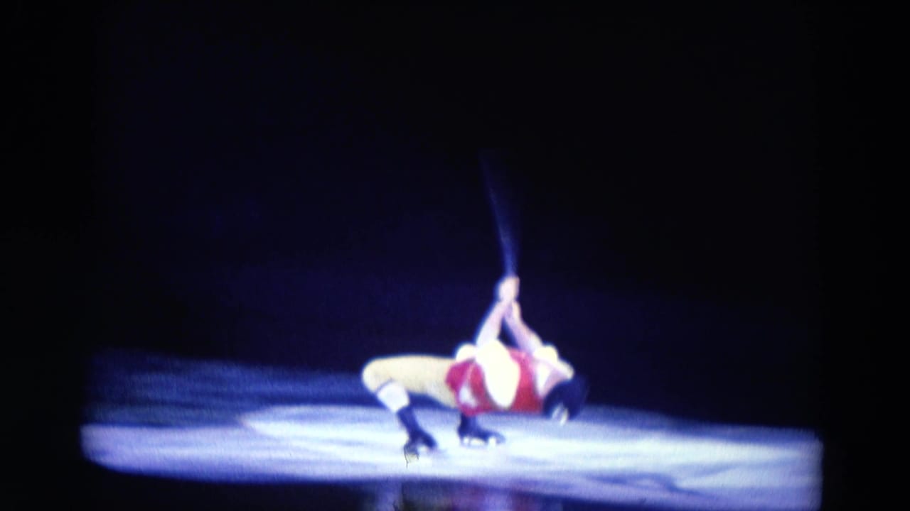 A costumed male skater continues a low backbend on the Chicago rink, one arm extended upward in blue light.