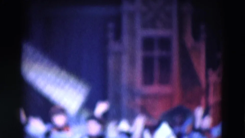 1969 Chicago 8mm frame showing a performer gesturing near the woman, with a theatrical house facade visible behind them.