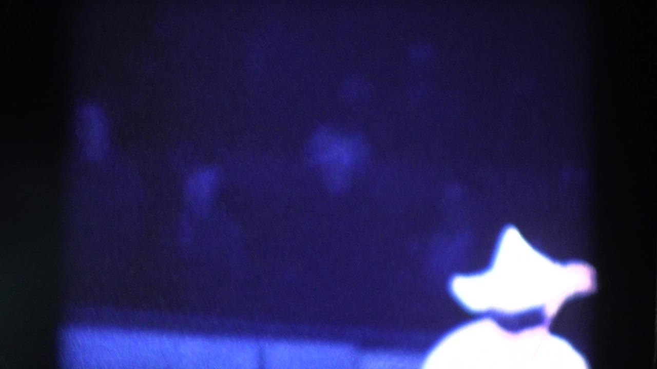 Ballerina in a bright headpiece and white costume on a dark stage.