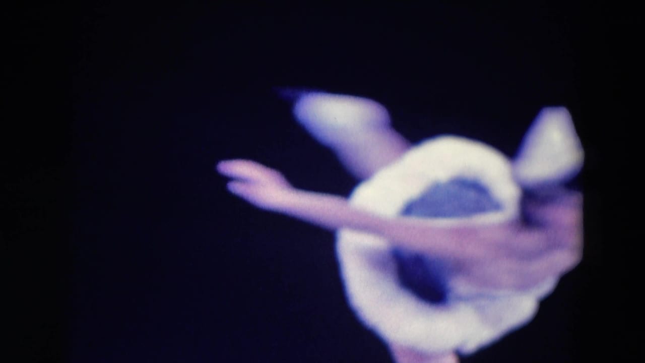 1969 Chicago 8mm frame showing a costumed ice skater in white mid-twirl, isolated against a dark background.
