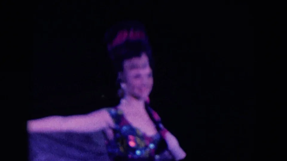 Costumed ice skater appears closer to camera in 1969 Chicago footage, arms spread and face softly visible under stage light.