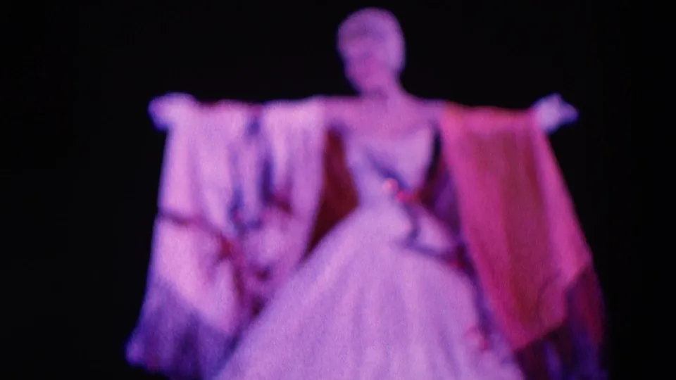 1969 Chicago 8mm frame showing two women in gowns with draped fabric under pink and purple stage light.