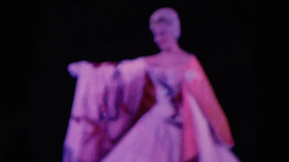 1969 Chicago 8mm frame of a woman in a pale gown holding fabric during a stage performance.