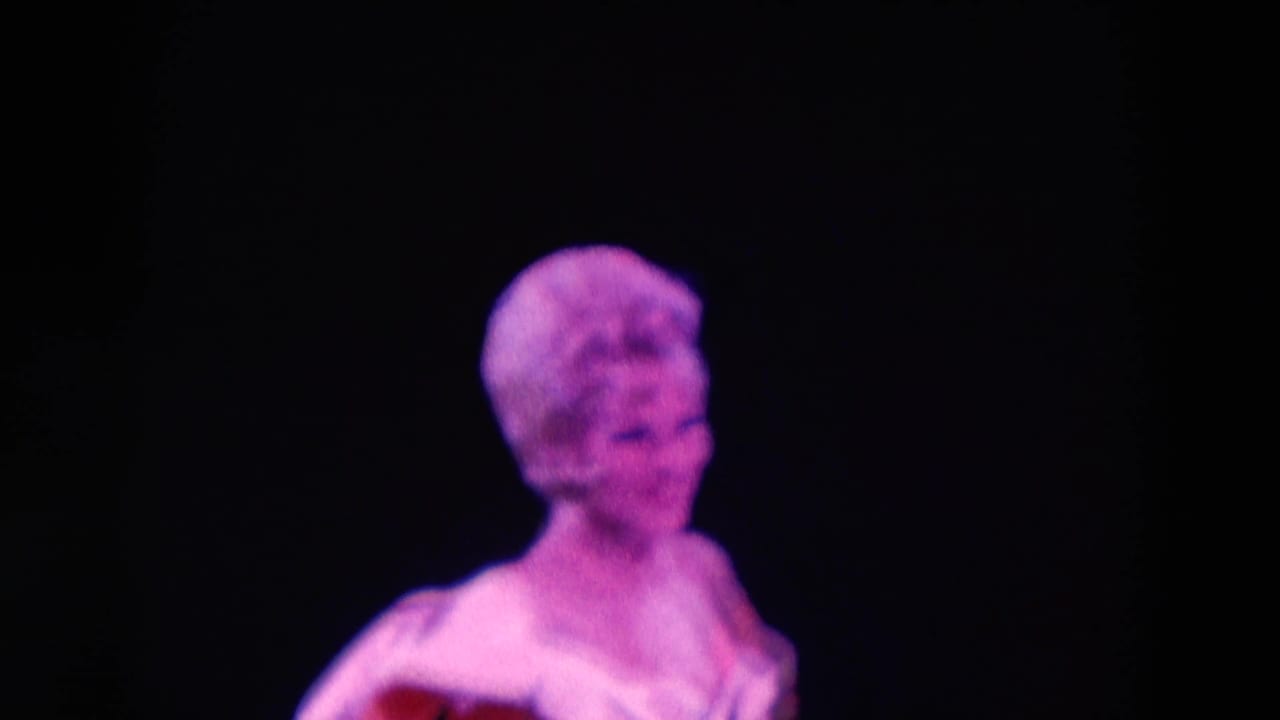 1969 Chicago 8mm frame with a short-haired female performer in colored stage light, seen against a black backdrop.