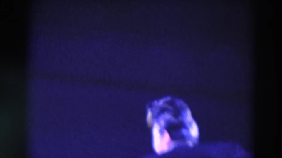 1969 Chicago 8mm frame with a male figure partly visible at the lower right, lit by blue stage light against darkness.