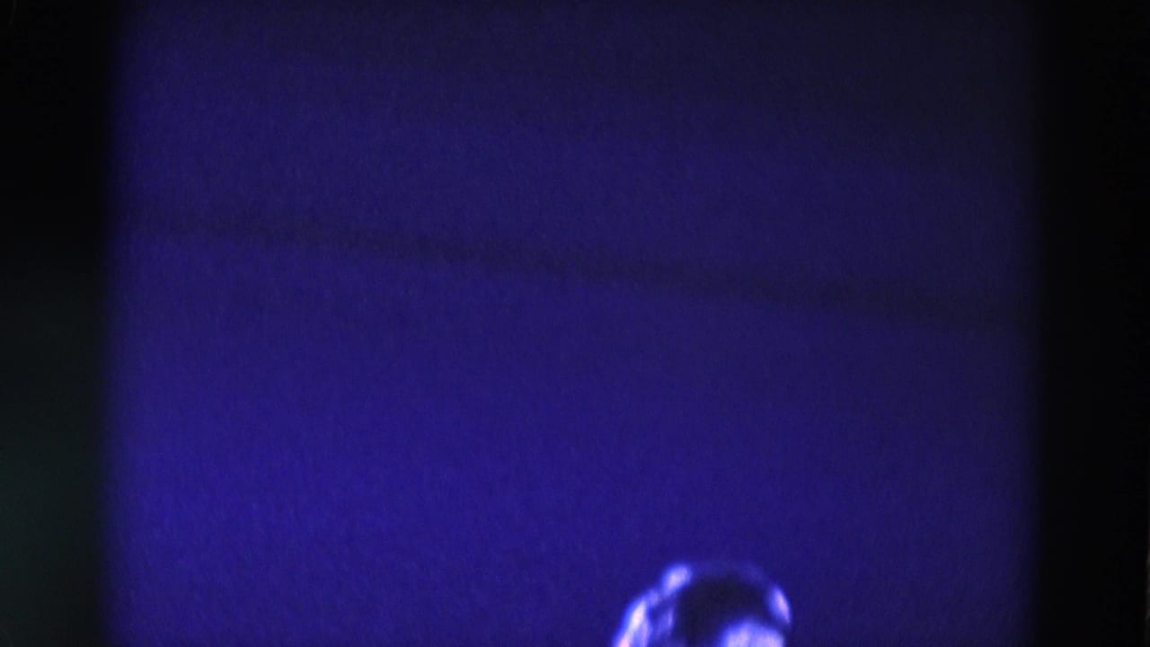 Dim blue-purple rink scene with a partially visible bright skater near the lower edge.