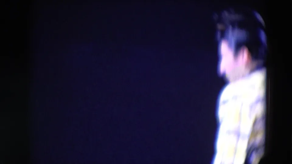 1969 Chicago 8mm frame showing a side view of a performer in a bright patterned shirt under blue stage light.