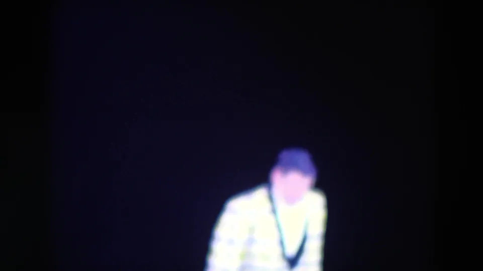 The performer bends or crouches on a dark stage, with the 8mm frame showing heavy contrast and blue-purple color shift.