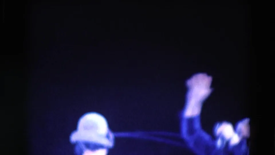 1969 Chicago 8mm frame showing a dark, blue-lit stage with a blurred capped or helmeted figure and a raised arm.