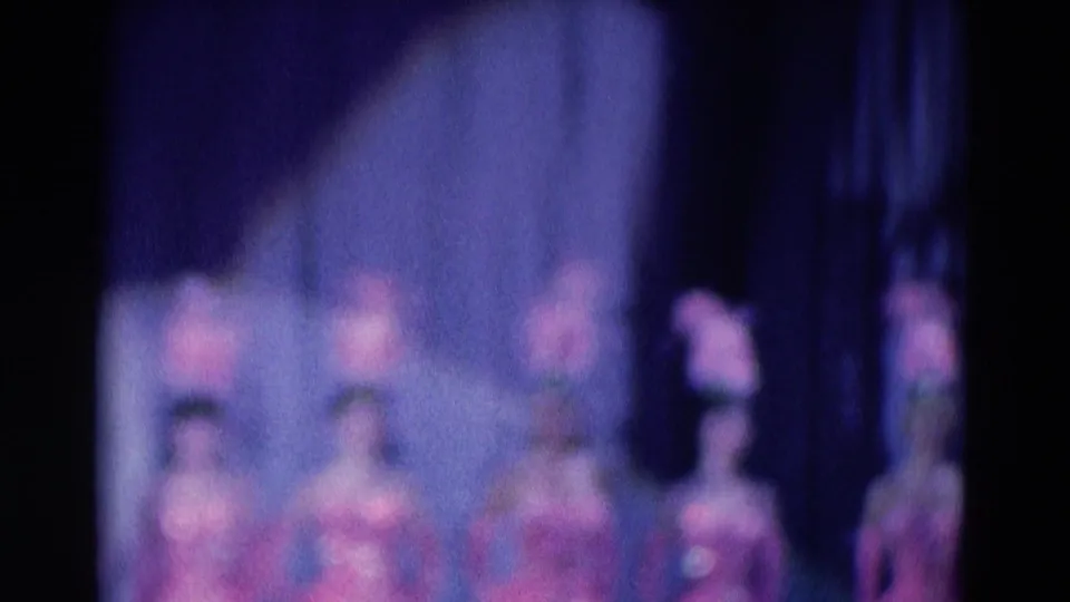 1969 Chicago 8mm frame showing several blurred dancers in pink costumes lined across a dim stage.
