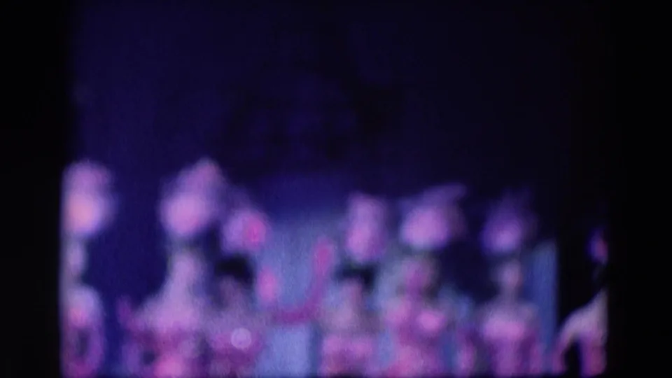 Grainy 1969 Chicago 8mm frame showing blurred dancers in pink costumes under purple-blue stage lighting.