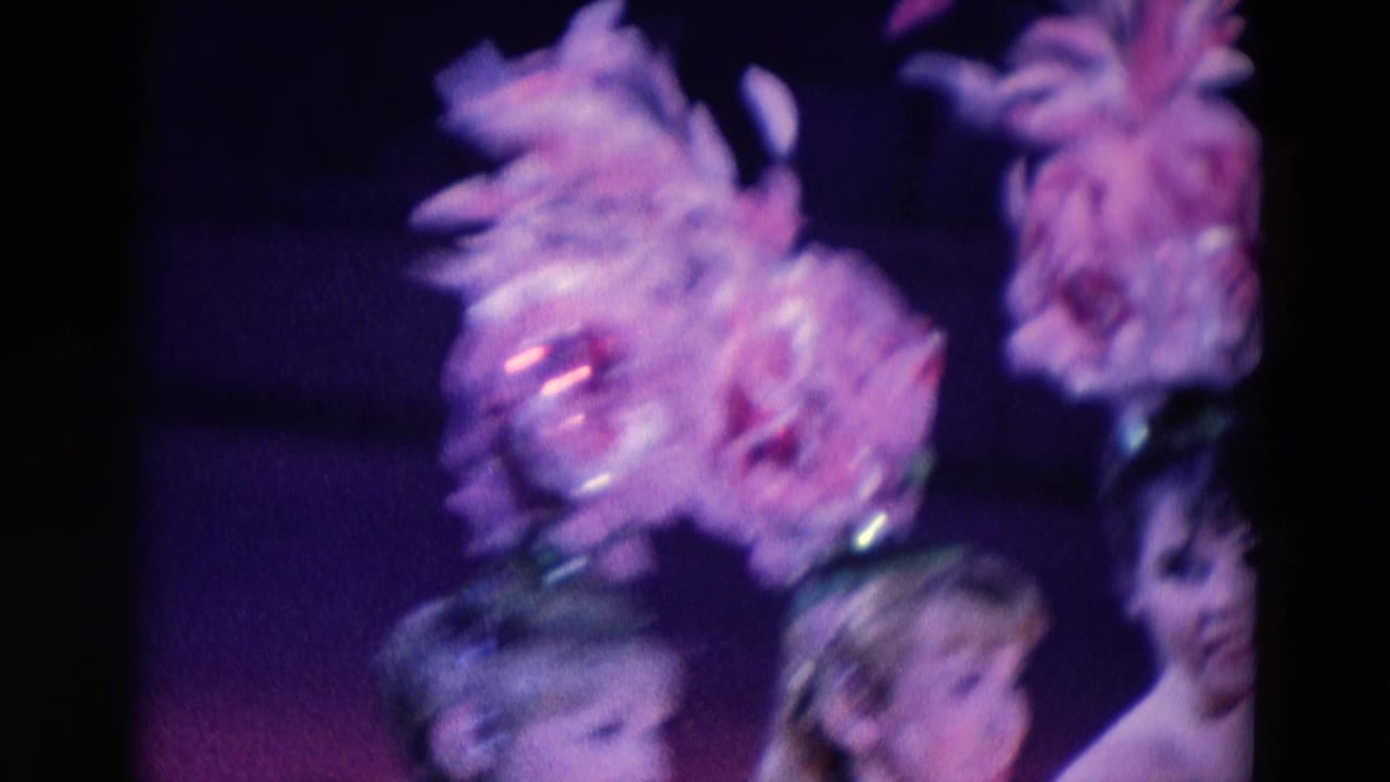 Women in feathered hats appear at the edge of a dark stage under purple light.