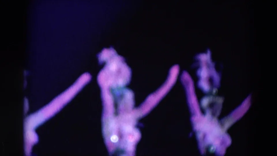 Final 1969 Chicago frame showing two women performers in feathered hats and sequined costumes during a purple-lit routine.