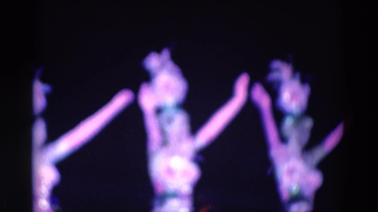 Blurred dancers under purple stage lighting with arms raised.