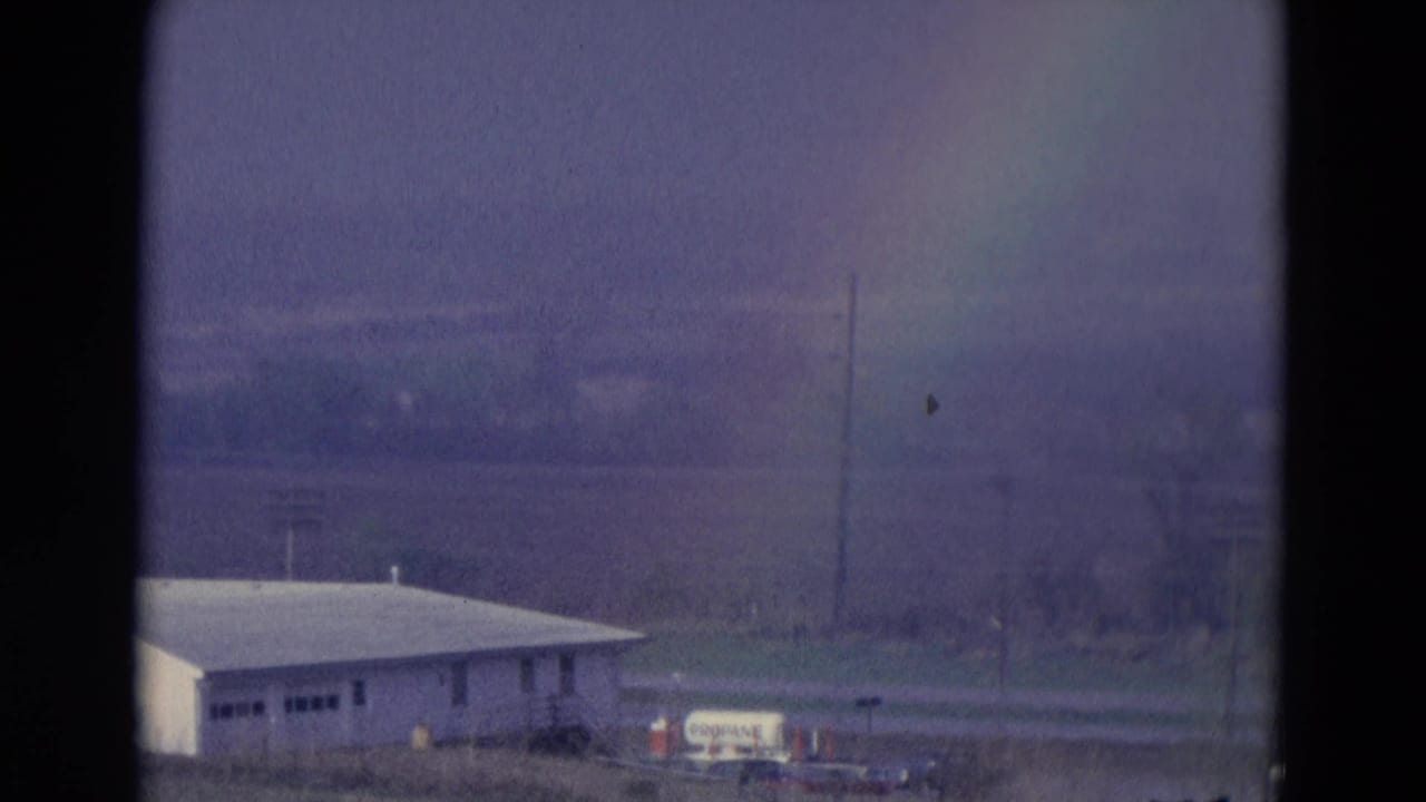 Faint rainbow above a white roadside building and utility poles under an overcast sky.