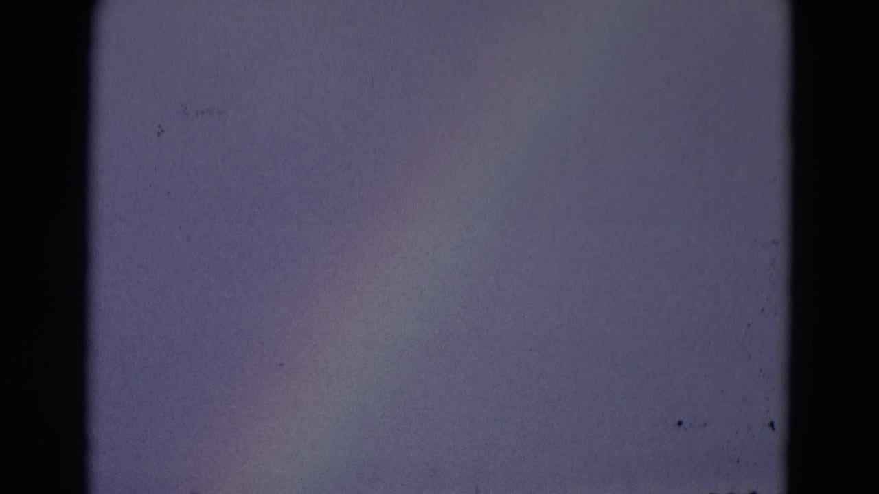 Soft rainbow band against a mostly empty gray-blue sky with film borders visible.