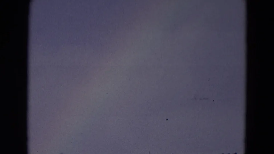 A dark, underexposed 8mm frame shows mostly overcast sky and film-frame edges during the rainbow shot.