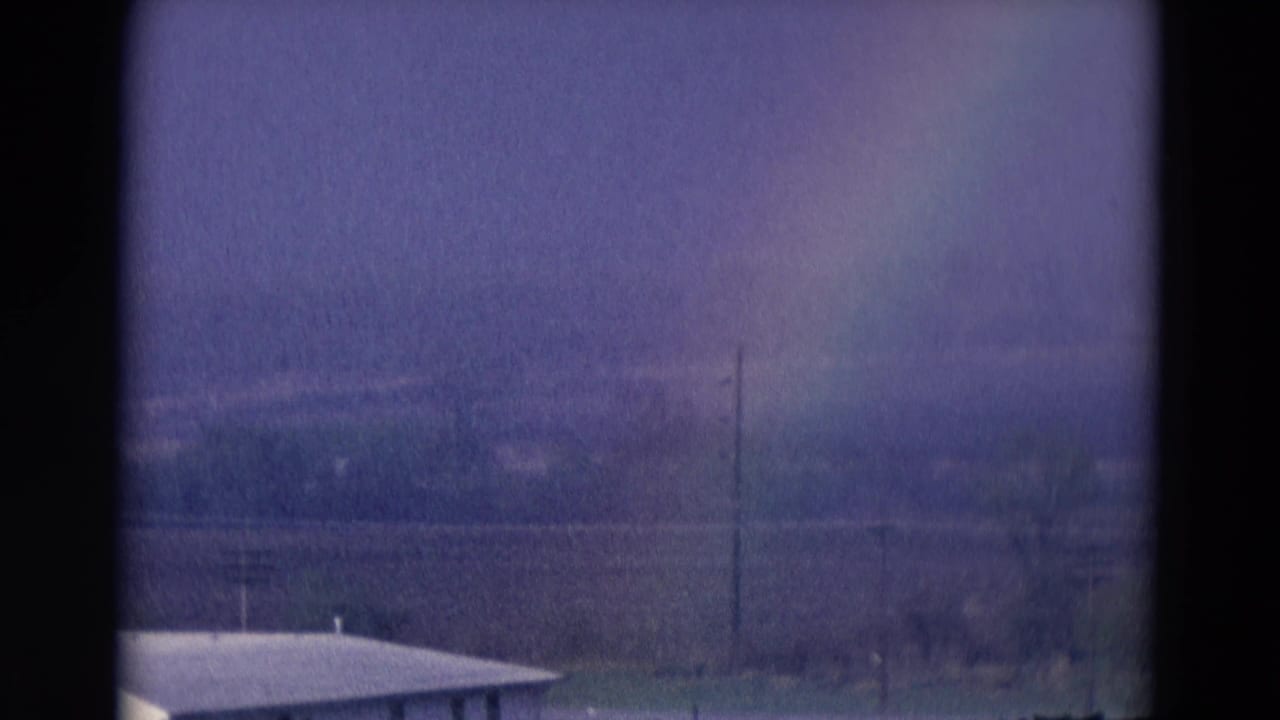 Distant marsh landscape under hazy sky with a faint vertical rainbow and film gate edges.