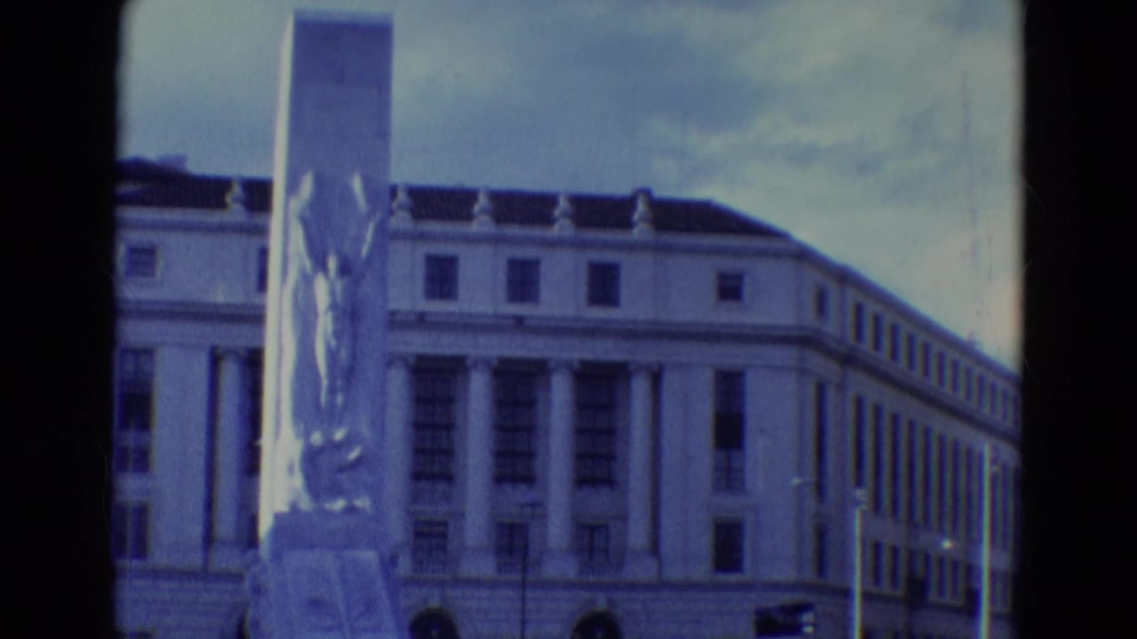 Columned public building with a tall monument in front, seen on soft 8mm color film.
