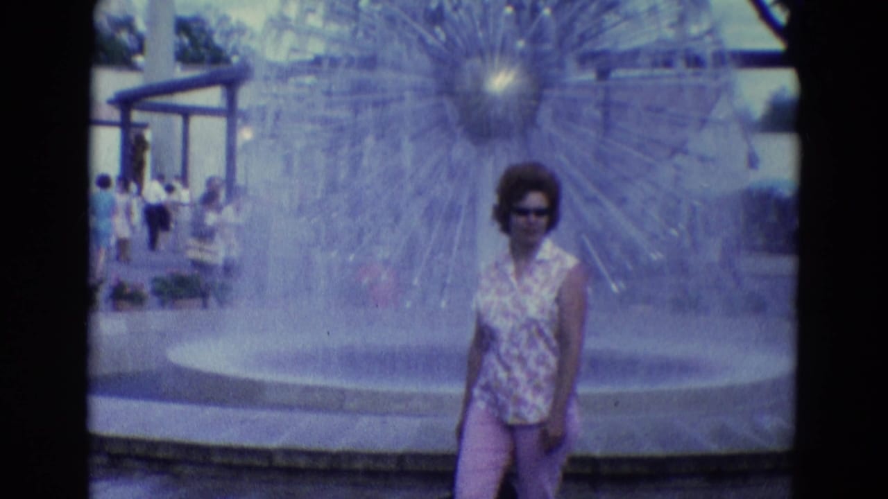 Woman in sunglasses stands near a large fountain at an amusement park.