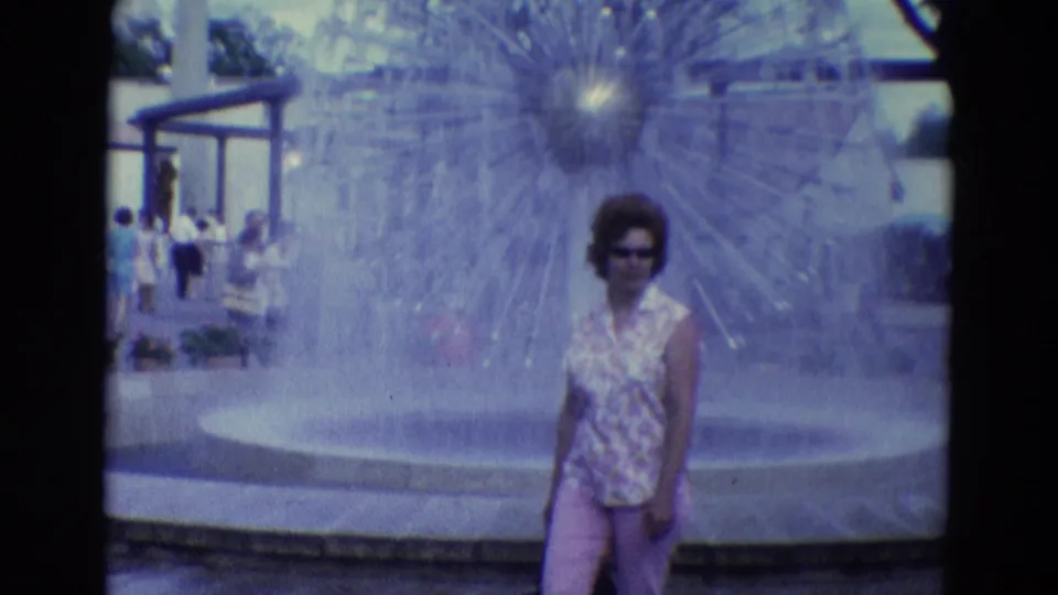 In the supplied 1969 Diller, Nebraska clip, a woman in sunglasses stands by a large spray fountain with park visitors nearby.