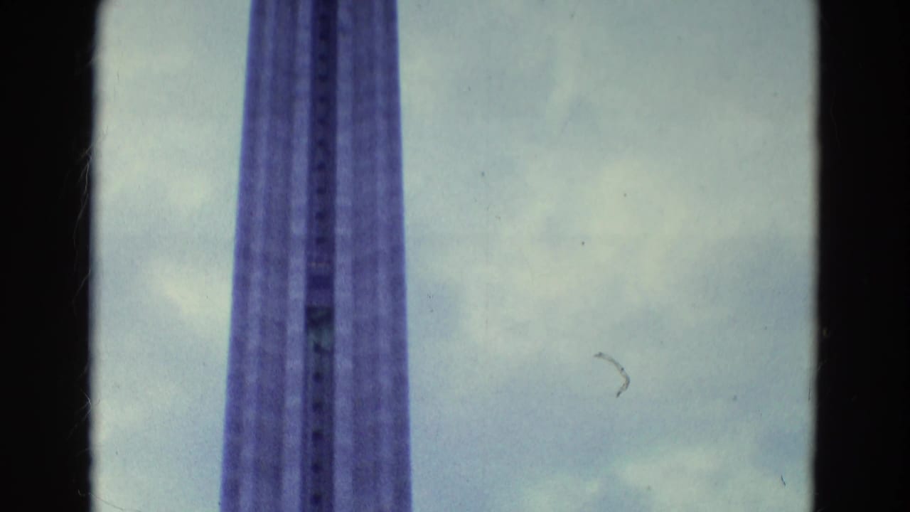 1969 8mm frame showing a tall observation-tower shaft viewed from below against a cloudy sky.