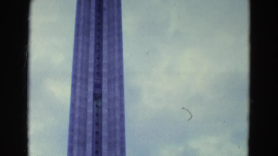 1969 8mm frame showing a tall observation-tower shaft viewed from below against a cloudy sky.