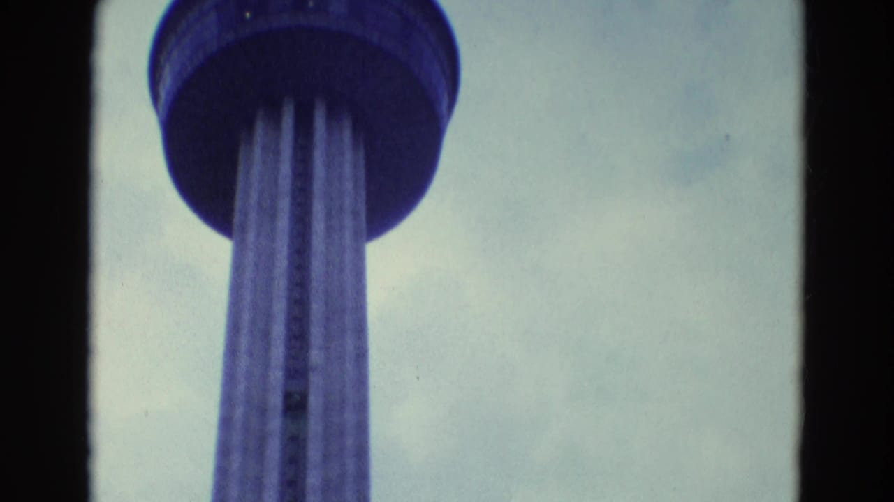 Low-angle view of a tall tower with circular observation deck against a cloudy sky.