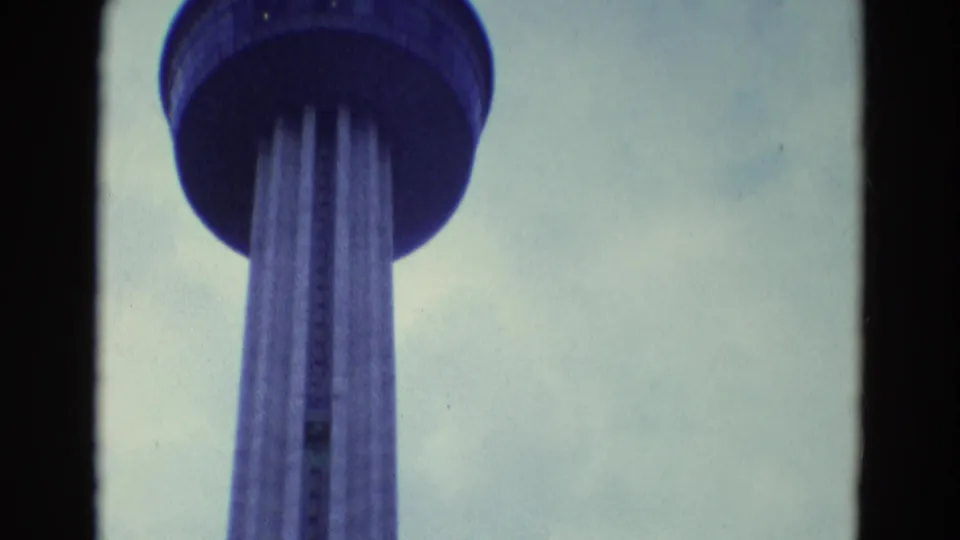 1969 Diller, Nebraska 8mm frame showing a low-angle view up a tall observation tower with a round deck and vertical columns.