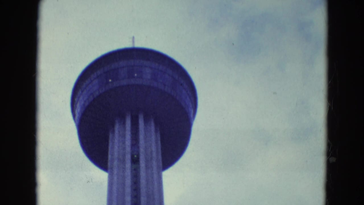 1969 8mm frame showing the Seattle Space Needle upper structure viewed from below against a cloudy sky.