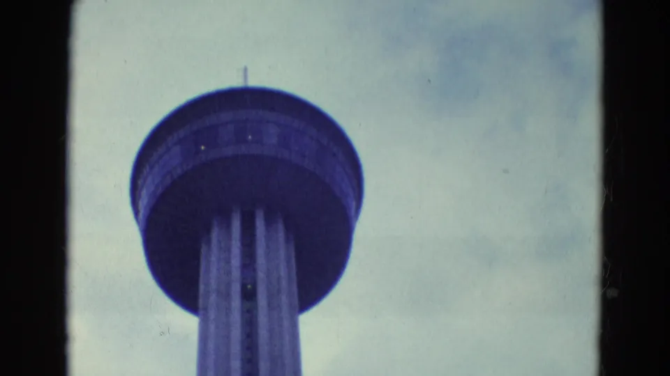 1969 8mm frame showing the Seattle Space Needle upper structure viewed from below against a cloudy sky.