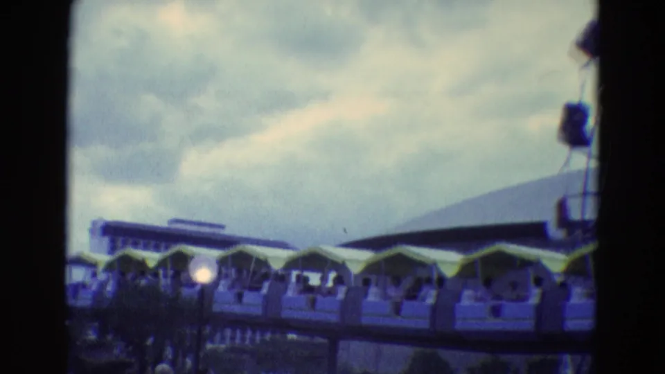1969 8mm fairground view with covered ride cars, lamps, and indistinct visitors near the lower frame.