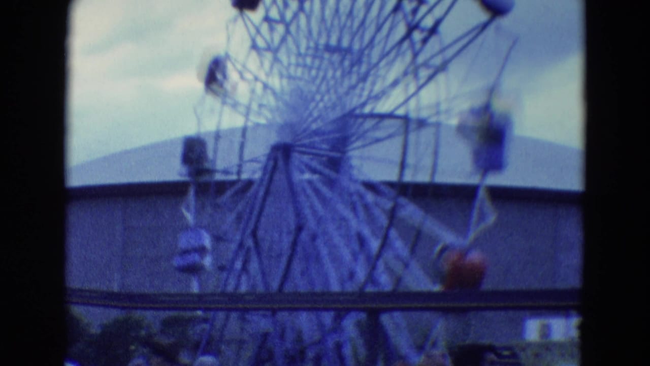 1969 Diller, Nebraska 8mm frame showing a distant spinning vertical amusement ride with passenger cars under an overcast sky.