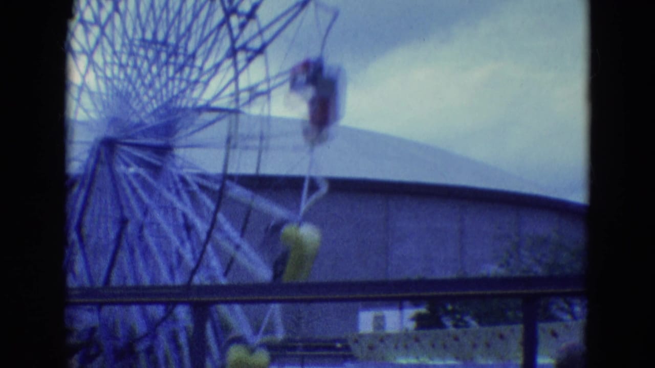 Amusement wheel with suspended cars partly obscured by dark film frame edges.