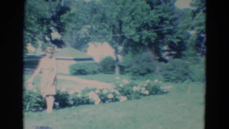 A woman in a pale dress walks beside the flowers, framed by a lawn, shrubs, and trees in Diller, Nebraska.