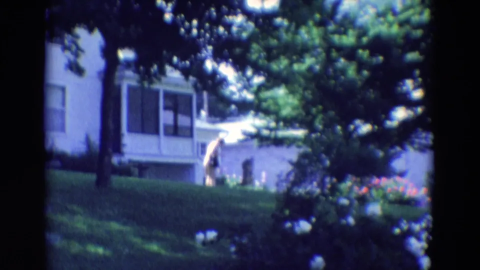 1969 Diller, Nebraska home-movie frame with a person in a yard before a white house, partly shaded by trees.