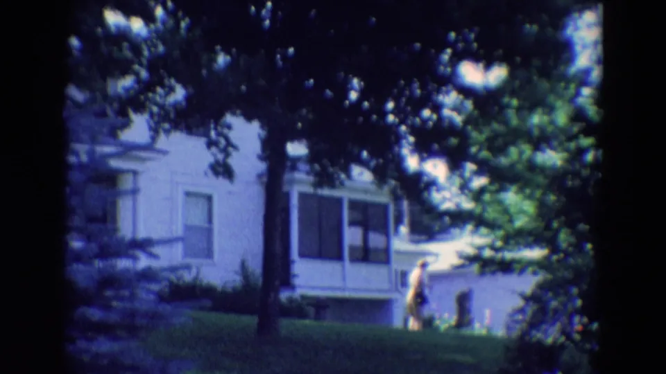 1969 Diller, Nebraska 8mm frame looking through shaded trees toward a white house and a person in the yard.