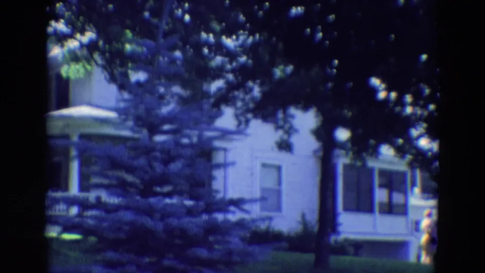 1969 Diller, Nebraska home-movie frame showing a two-story white house behind trees with a porch and front yard.