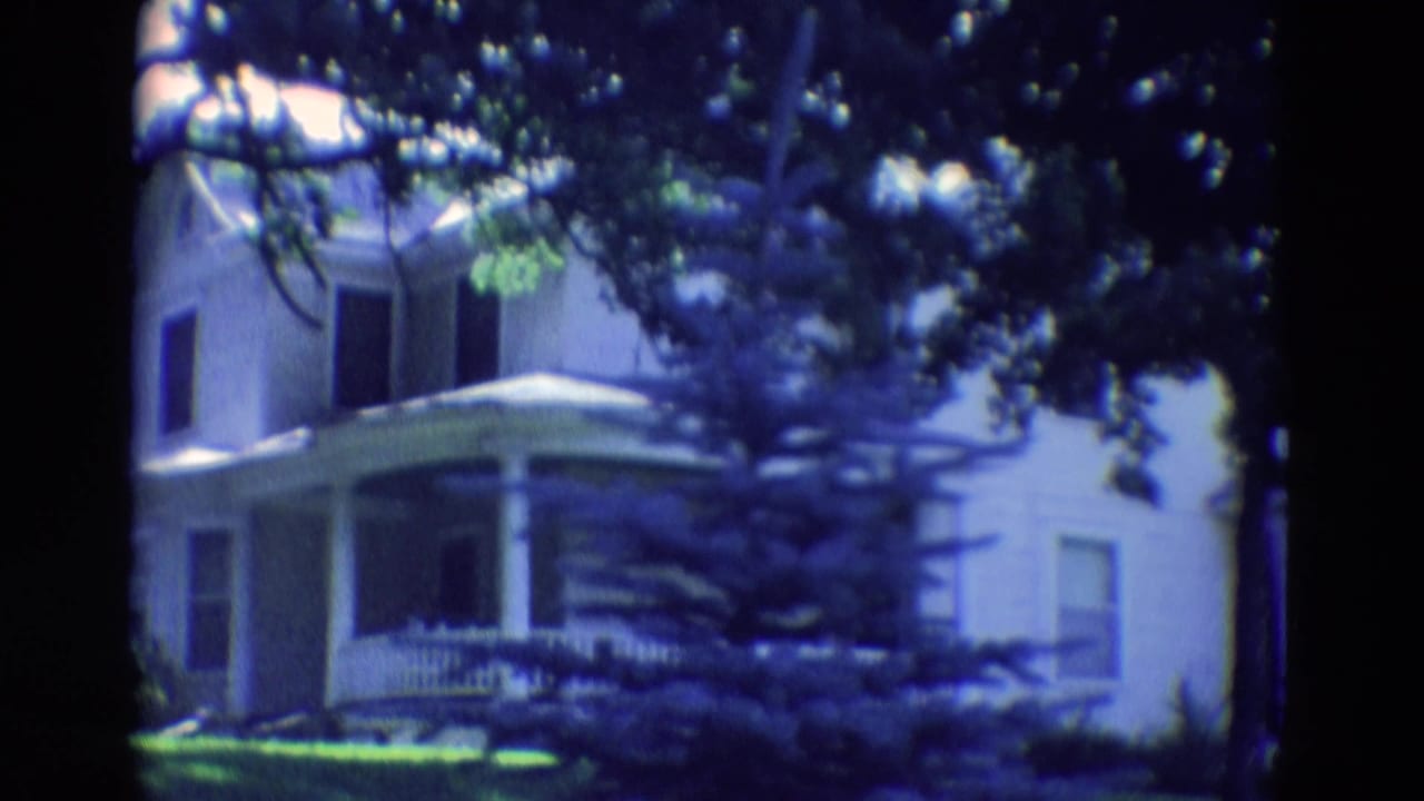 White house exterior framed by dark tree branches and a front porch.