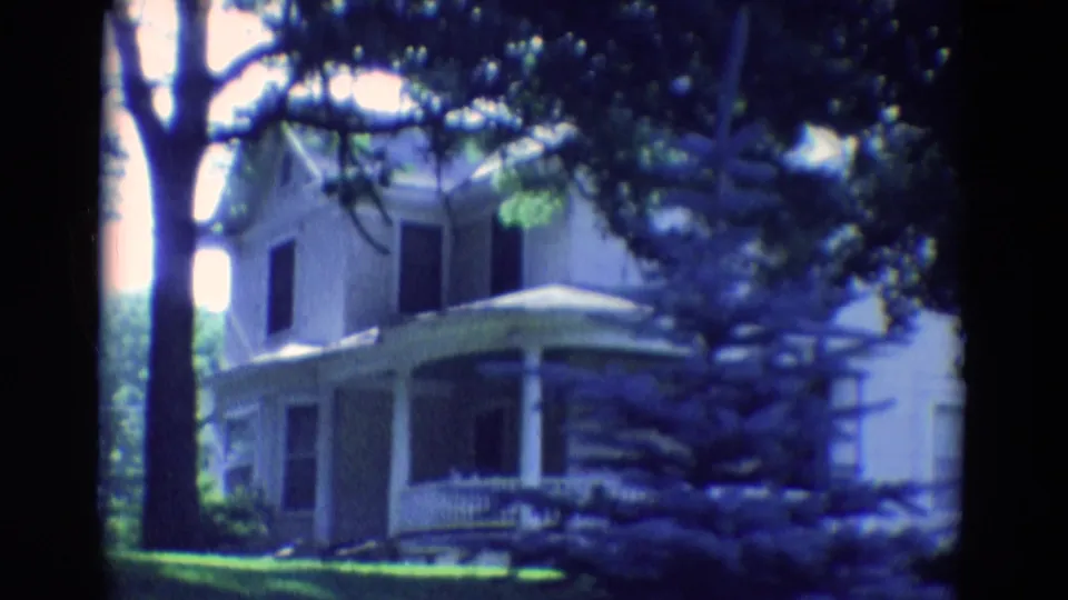 1969 Diller, Nebraska home-movie still with the house closer in frame, showing porch details beneath large trees.