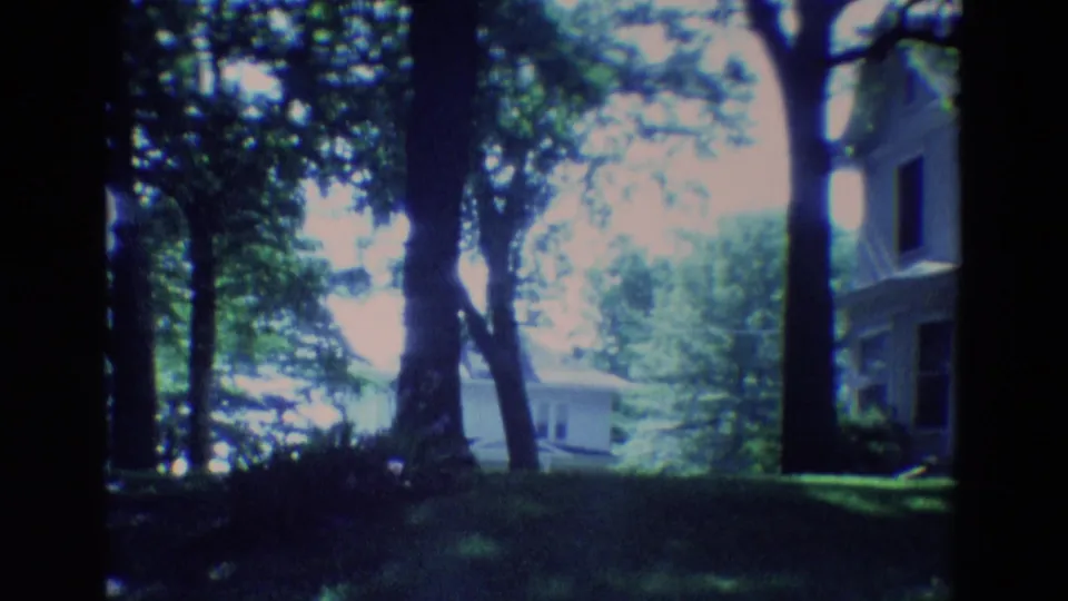 1969 Diller, Nebraska 8mm frame with mature trees, shaded lawn, part of a house, and a small structure beyond the yard.