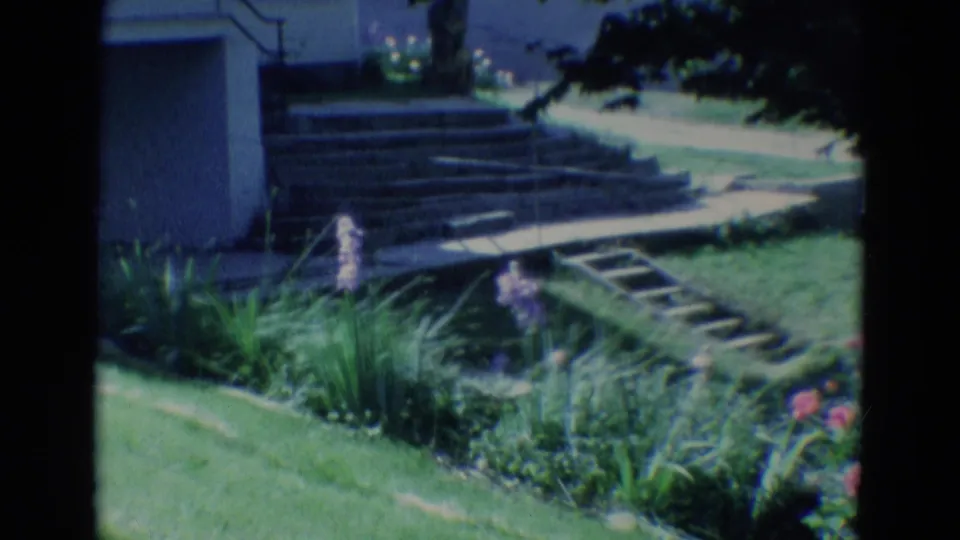 1969 Diller, Nebraska home exterior with siding, steps, a small ladder, lawn, and flower beds in soft 8mm color.